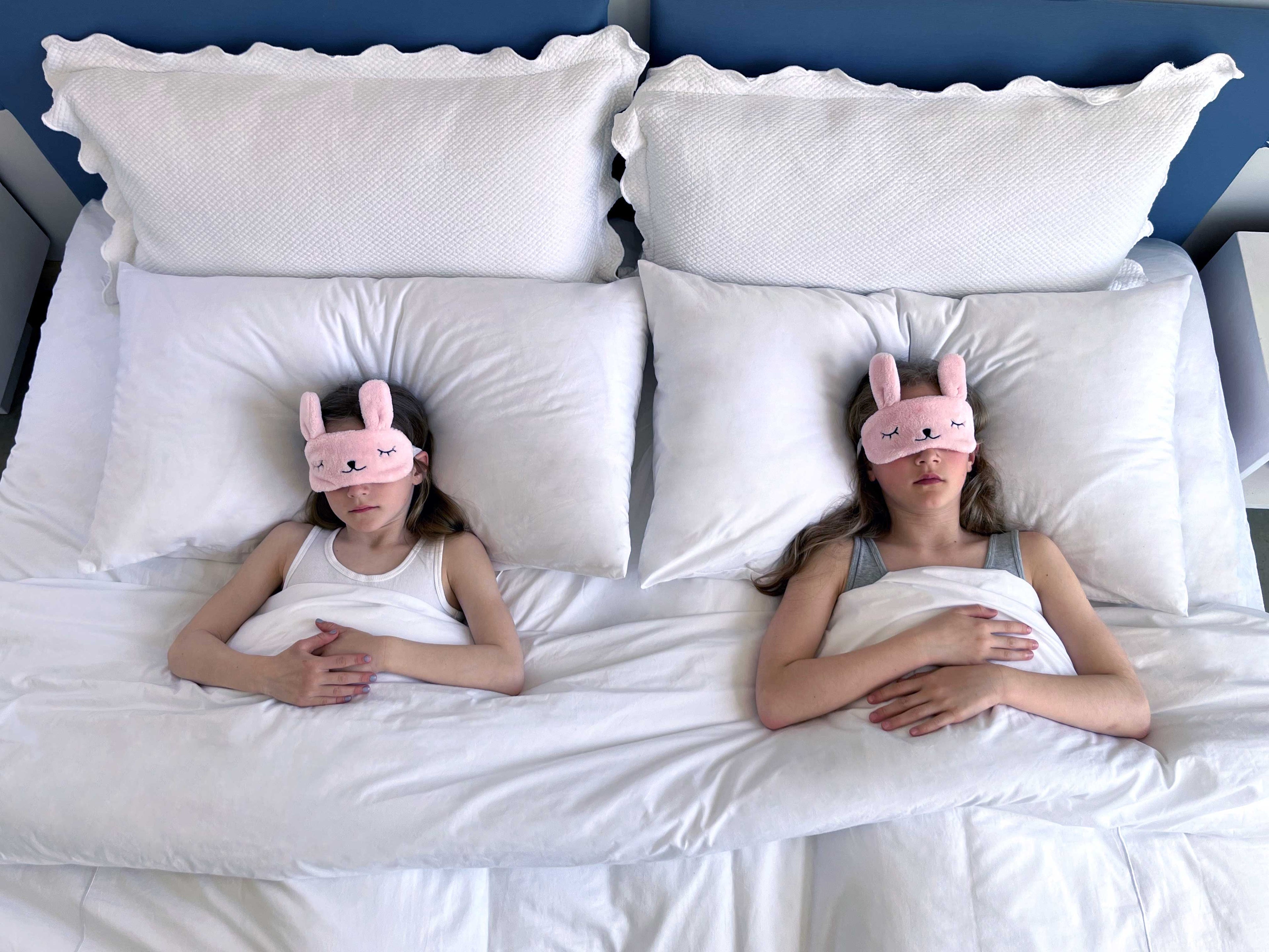 Deux jeunes filles couchées dans lit blanc avec un bandeau rose sur les yeux