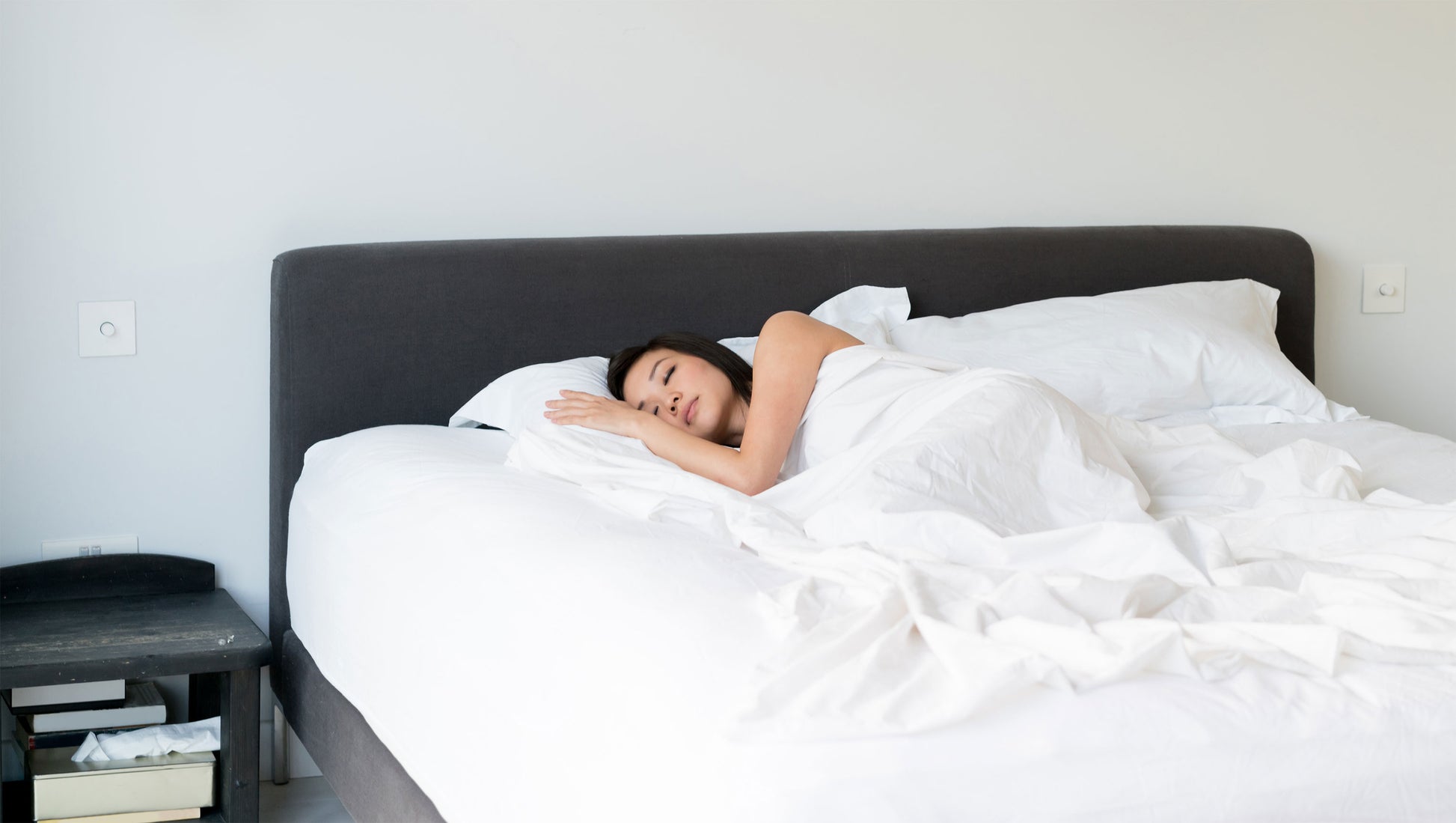 Femme couchée dans un lit blanc avec une table de chevet noire