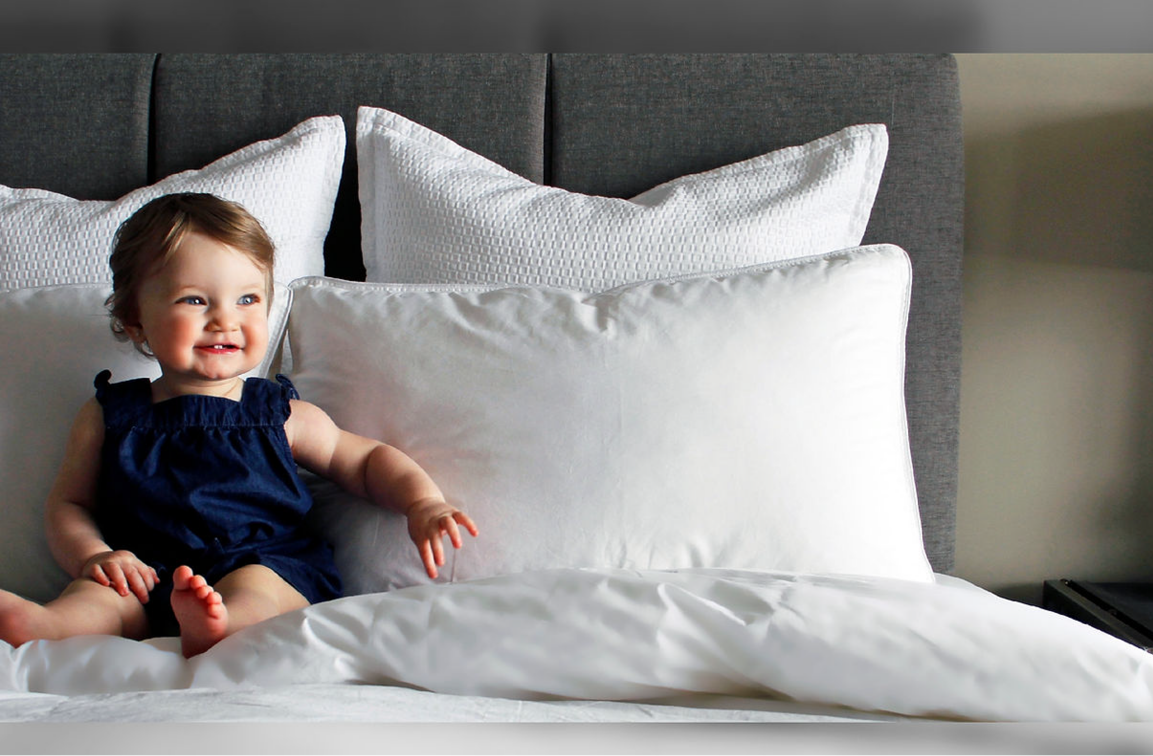 Bébé assis sur un lit blanc appuyé sur des oreillers