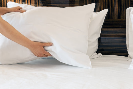  Bras tenant une oreiller blanche dans un lit blanc