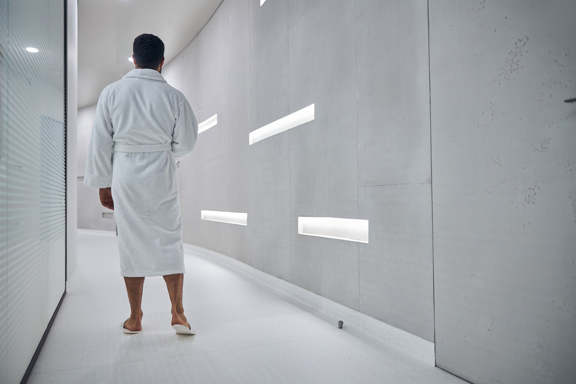 Homme portant un peignoir blanc dans un corridor éclairé gris