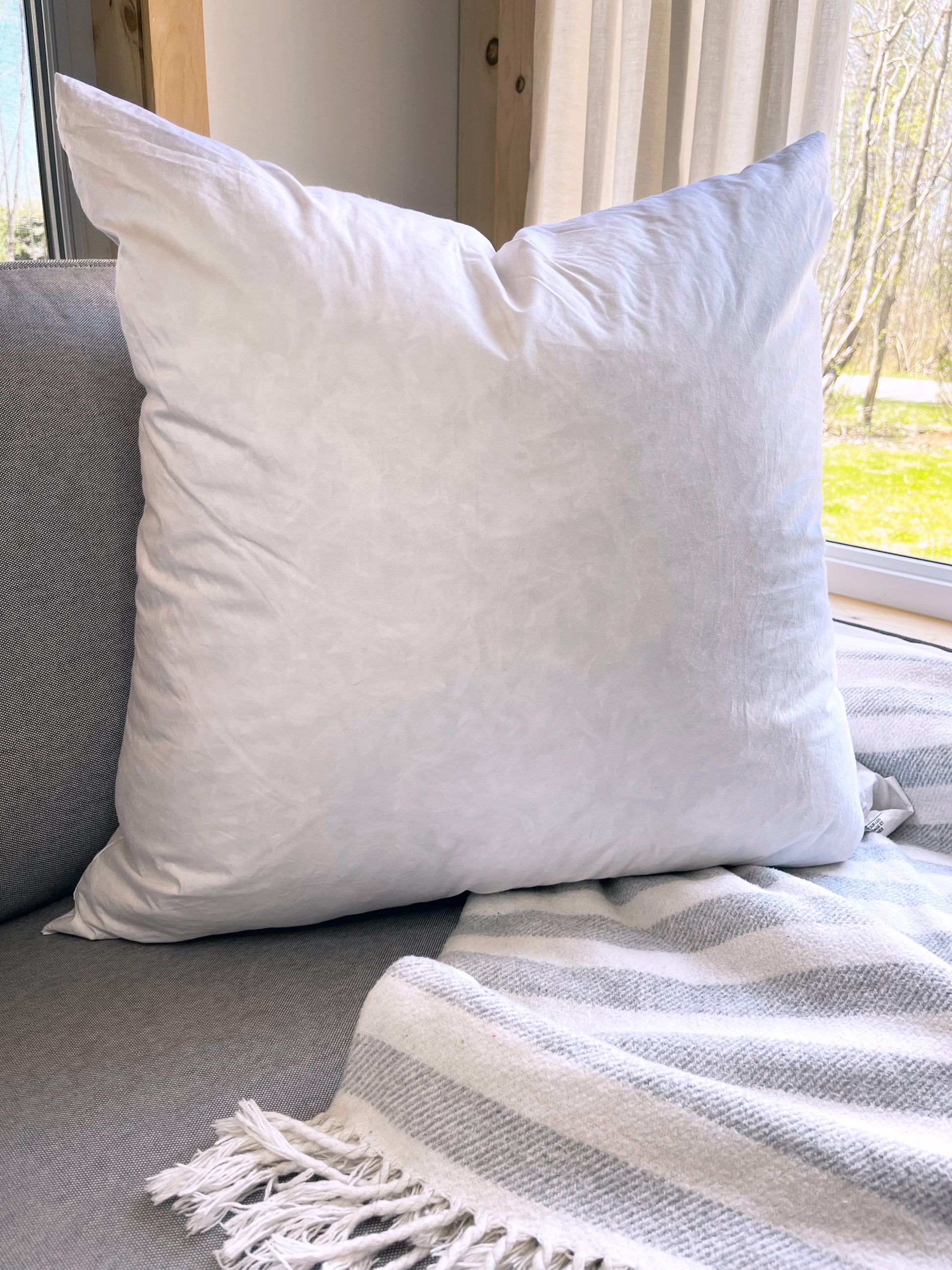 Coussin blanc sur un sofa avec une jeté sur le divan en avant d'une fenêtre donnant sur l'extérieur.